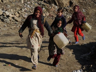 Niños afganos corriendo con botellas de plástico vacías para rellenarlas con...