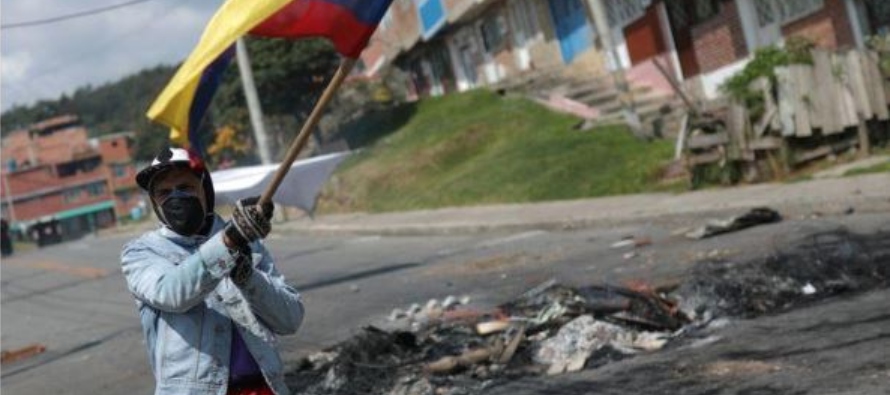 Un hombre, usanso tapabocas, bate una bandera de Colombia durante una protesta de habitantes pobres...