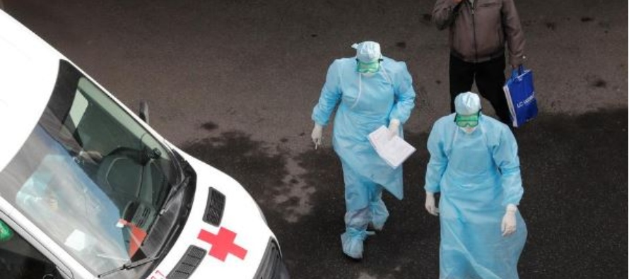 Foto del lunes de un hombre usando una mascarilla camina detrás de dos médicos fuera...