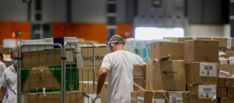 Trabajadores sanitarios protegidos con mascarilla mueven cajas en el interior del almacén...