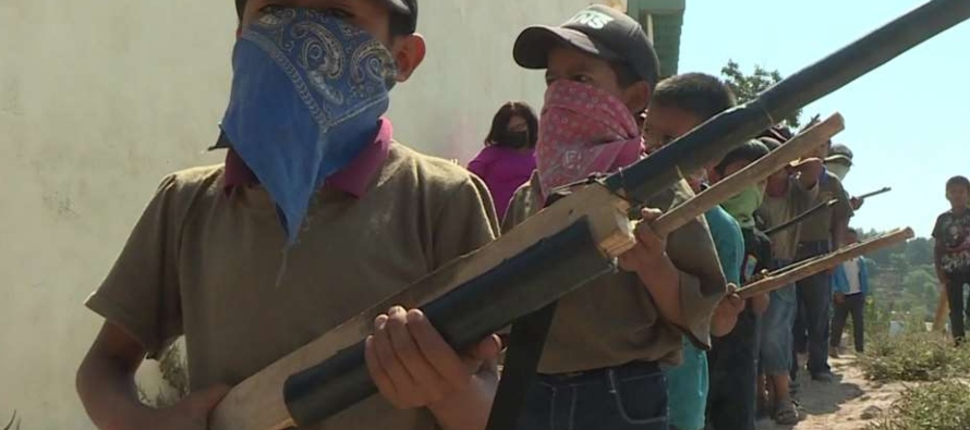 Le siguen una treintena de niños de seis a doce años con rifles de madera o varas que...